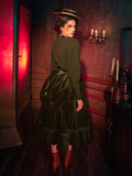 The haunting beauty of the Victorian Velvet Bustle Skirt in Olive comes to life as models show it off for La Femme en Noir, the renowned gothic clothing brand.