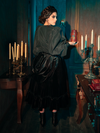 The dark allure of the Victorian Velvet Bustle Skirt in Black is skillfully portrayed by models showcasing the hauntingly gorgeous design for La Femme en Noir.
