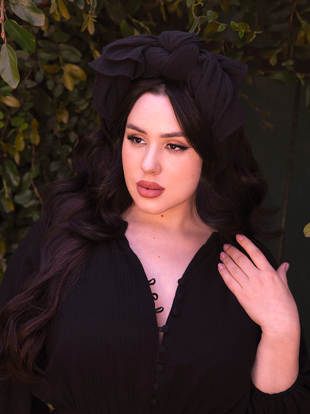 Step into the enigmatic world of La Femme en Noir Clothing and witness the ethereal sight of a beautiful model donning the Coven Head Wrap in Black, an alluring accessory that weaves a tapestry of gothic elegance.