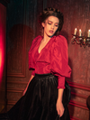 With an aura of gothic elegance, female models strike various poses while presenting the Taffeta Edwardian Blouse in Crimson Red.