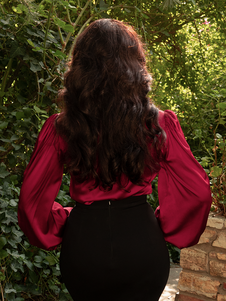 In deep red satin, she commands attention, her blouse an ode to confidence wrapped in Victorian grace.