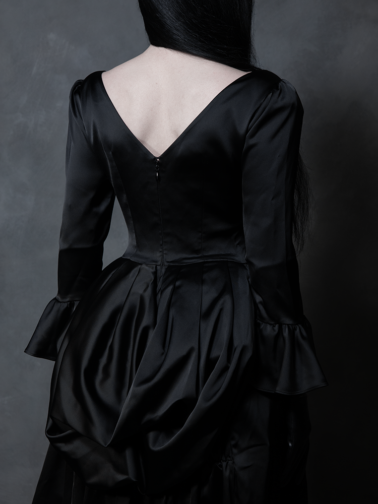 Exuding classic Whimsigoth charm, a female model showcases a stunning black satin gothic dress designed for ultimate dark romance.