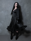A female model highlights a dramatic Whimsigoth style vibe while wearing a flowing black satin dress rich with dark elegance.