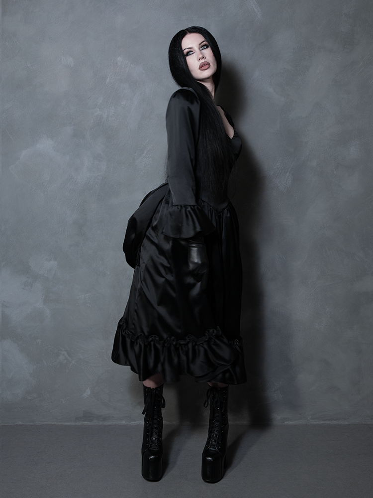 A female model evokes a timeless, poetic atmosphere while dressed in a black satin gown of pure gothic glamour.