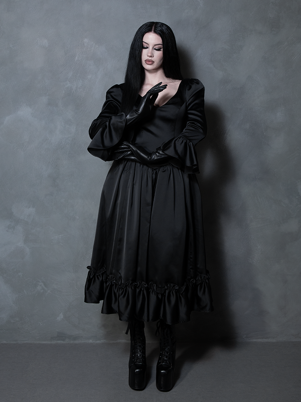 A female model channels an ethereal Whimsigoth fantasy, wearing a rich black satin gown that defines gothic glamour.