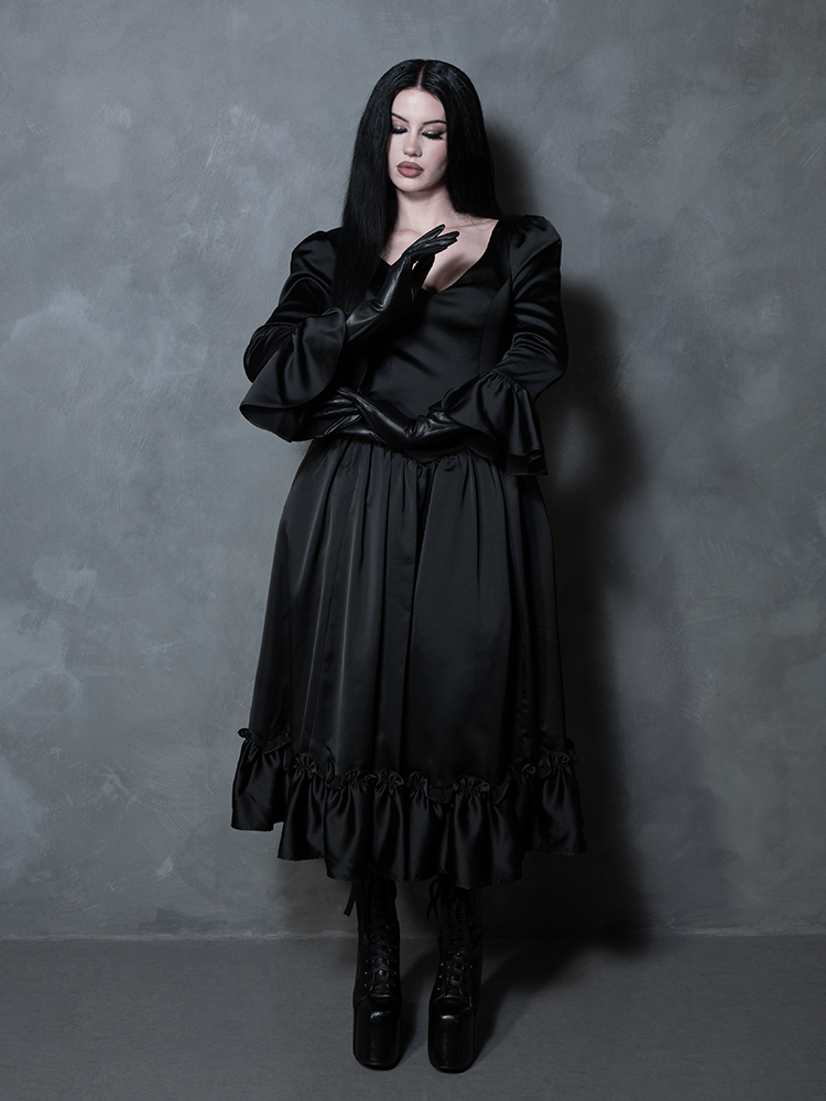 A female model channels an ethereal Whimsigoth fantasy, wearing a rich black satin gown that defines gothic glamour.