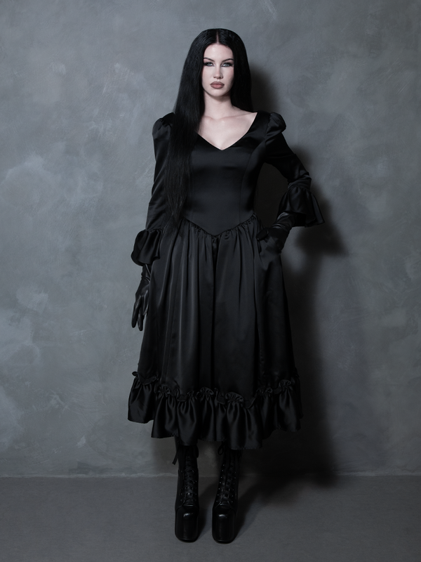 A gorgeous representation of dark elegance, a female model wears a sleek black satin dress tailored for the modern Victorian Goth.