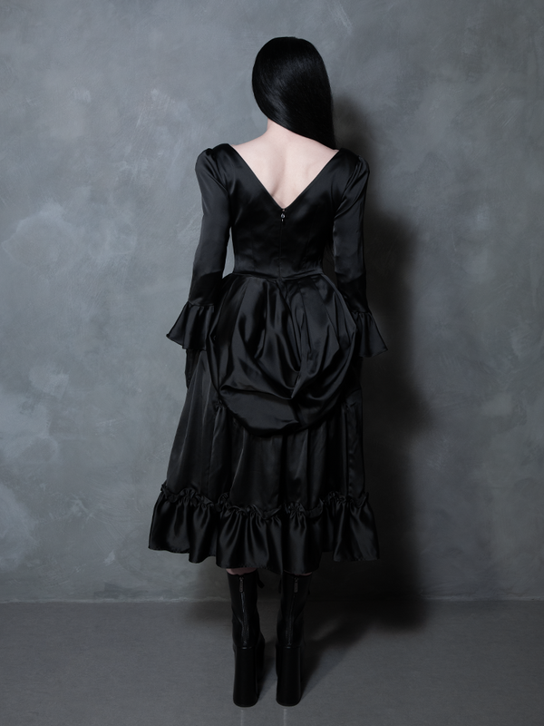 A female model brings an element of theatrical dark romance to life, wearing a striking black satin dress with gothic glamour.