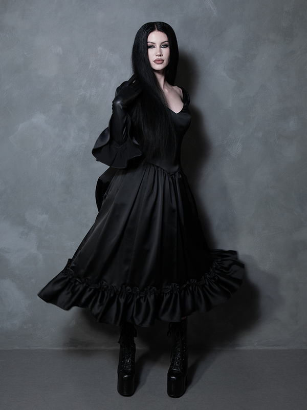 The epitome of gothic clothing at its finest, a female model wears a majestic black satin dress steeped in dark romance.