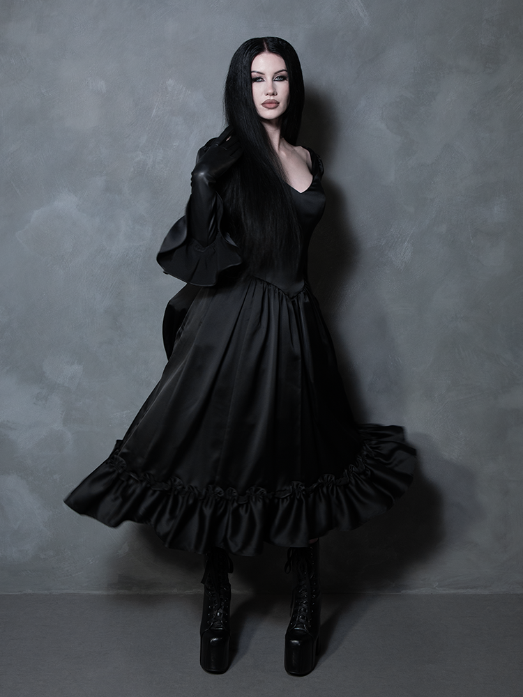 The epitome of gothic clothing at its finest, a female model wears a majestic black satin dress steeped in dark romance.