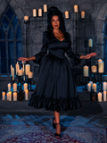 In the haunting embrace of candlelight, the enchanting female model parades the Ebony Rapture Velvet Bustier Gown, a masterpiece from the ethereal realm of gothic fashion conjured by La Femme en Noir.