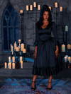 Cloaked in the somber aura of candlelight, the alluring maiden dons the Gothic Noir Satin Bustle Dress in Onyx, a masterpiece of gothic elegance crafted by the enchanting hands of La Femme en Noir.
