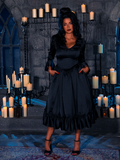 Immersed in the eerie ambiance of candlelight, the beguiling female model presents the Abyssal Romance Satin Bustle Dress, an opus of gothic allure from the evocative atelier of La Femme en Noir.