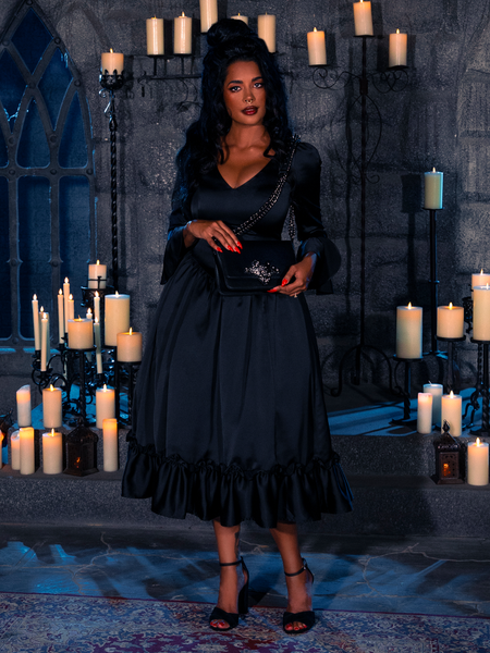 Within the dimly lit chamber, lit solely by the ethereal glow of candles, the resplendent damsel unveils the Noir Veil of Temptation Satin Bustle Dress from the haunting repertoire of the gothic couturier, La Femme en Noir.
