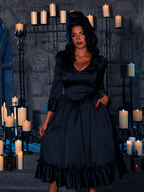 Within the dimly illuminated chamber, the exquisite model gracefully presents the Ebony Elegance Silk Bustle Gown by the gothic couturier, La Femme en Noir.