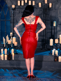 Micheline Pitt radiates the spirit of gothic clothing as she dons the BRAM STOKER'S DRACULA Quilted Order of the Dragon Armor Skater Skirt in Blood Red Vegan Leather, a striking creation from the goth clothing brand La Femme en Noir, within the ambiance of a candle-lit dungeon.