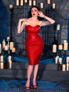 Micheline Pitt embraces the dark allure of gothic fashion with the BRAM STOKER'S DRACULA Quilted Order of the Dragon Armor Skater Skirt in Blood Red Vegan Leather, a masterpiece from La Femme en Noir's goth clothing assortment, while posing in a dungeon illuminated by candles.