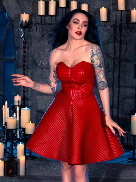 Micheline Pitt strikes a pose in a dimly lit dungeon, donning the BRAM STOKER'S DRACULA Quilted Order of the Dragon Armor Skater Skirt in Blood Red Vegan Leather, courtesy of the gothic apparel brand La Femme en Noir.