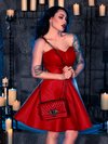 Micheline Pitt steps into a candle-lit dungeon, exuding the essence of gothic fashion in the BRAM STOKER'S DRACULA Quilted Order of the Dragon Armor Skater Skirt in Blood Red Vegan Leather, a masterpiece from La Femme en Noir's goth clothing line.