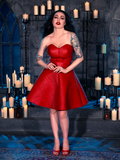 Micheline Pitt embraces the dark allure of gothic fashion with the BRAM STOKER'S DRACULA Quilted Order of the Dragon Armor Skater Skirt in Blood Red Vegan Leather, a masterpiece from La Femme en Noir's collection, while posing in a candle-lit dungeon.