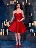 Micheline Pitt, dressed in the BRAM STOKER'S DRACULA Quilted Order of the Dragon Armor Skater Skirt in Blood Red Vegan Leather from La Femme en Noir's goth clothing line, poses in a moody, candle-lit dungeon.