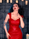 In the goth clothing masterpiece, the BRAM STOKER'S DRACULA Quilted Order of the Dragon Armor Bustier Top in Blood Red Vegan Leather, Micheline Pitt strikes a captivating pose in a candle-lit dungeon, a testament to La Femme en Noir's unique style.