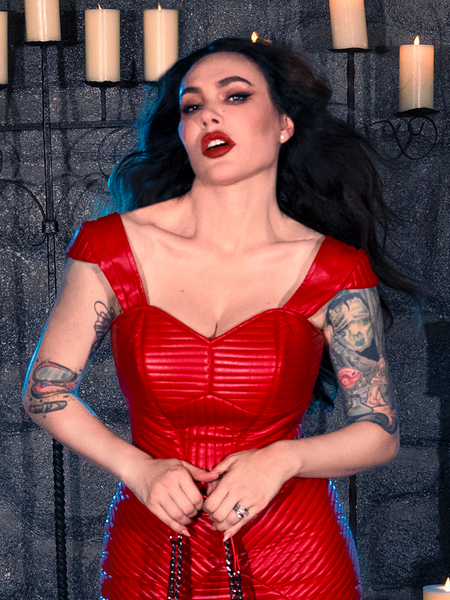 Micheline Pitt embodies the essence of gothic fashion in the BRAM STOKER'S DRACULA Quilted Order of the Dragon Armor Bustier Top in Blood Red Vegan Leather, showcasing her dark elegance within a candle-lit dungeon, courtesy of the goth clothing brand La Femme en Noir.