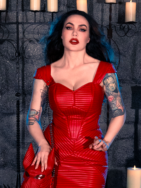 Within a candlelit dungeon, Micheline Pitt evokes the mystique of gothic clothing while adorned in the BRAM STOKER'S DRACULA Quilted Order of the Dragon Armor Bustier Top in Blood Red Vegan Leather, a masterpiece from La Femme en Noir's goth clothing collection.