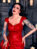 Wearing the BRAM STOKER'S DRACULA Quilted Order of the Dragon Armor Bustier Top in Blood Red Vegan Leather, Micheline Pitt radiates the essence of gothic fashion within a candle-lit dungeon, attired by the esteemed goth clothing brand La Femme en Noir.