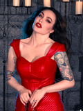 Micheline Pitt embraces the enigmatic allure of gothic clothing as she dons the BRAM STOKER'S DRACULA Quilted Order of the Dragon Armor Bustier Top in Blood Red Vegan Leather, a creation from La Femme en Noir's gothic fashion collection, while posing in a candlelit dungeon.