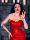 Micheline Pitt strikes a pose in a candle-lit dungeon, adorned in the BRAM STOKER'S DRACULA Quilted Order of the Dragon Armor Bustier Top in Blood Red Vegan Leather, courtesy of La Femme en Noir, a renowned gothic clothing brand.