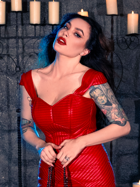 In a candlelit dungeon, Micheline Pitt showcases her affinity for dark fashion by wearing the BRAM STOKER'S DRACULA Quilted Order of the Dragon Armor Bustier Top in Blood Red Vegan Leather, a standout piece from the gothic apparel line of La Femme en Noir.