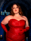In the goth clothing masterpiece, the BRAM STOKER'S DRACULA Quilted Order of the Dragon Armor Bustier Top in Blood Red Vegan Leather, red-haired female model strikes a captivating pose in a candle-lit dungeon, a testament to La Femme en Noir's unique style.