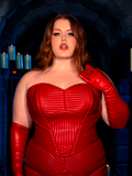 Within a candlelit dungeon, female red-haired model evokes the mystique of gothic clothing while adorned in the BRAM STOKER'S DRACULA Quilted Order of the Dragon Armor Bustier Top in Blood Red Vegan Leather, a masterpiece from La Femme en Noir's goth clothing collection.