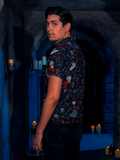 Against the backdrop of a candle-lit dungeon, the model rocks the BRAM STOKER'S DRACULA Button Up Short Sleeve Shirt featuring Dracula Novelty Print.