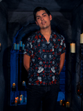 With the dungeon bathed in candlelight, the model wears the BRAM STOKER'S DRACULA Button Up Short Sleeve Shirt adorned with Dracula Novelty Print.
