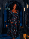 An exquisite model strikes a pose in a dimly lit dungeon, adorned in the BRAM STOKER'S DRACULA Gothic Tales Swing Dress in Dracula Novelty Print by the goth fashion brand La Femme en Noir.
