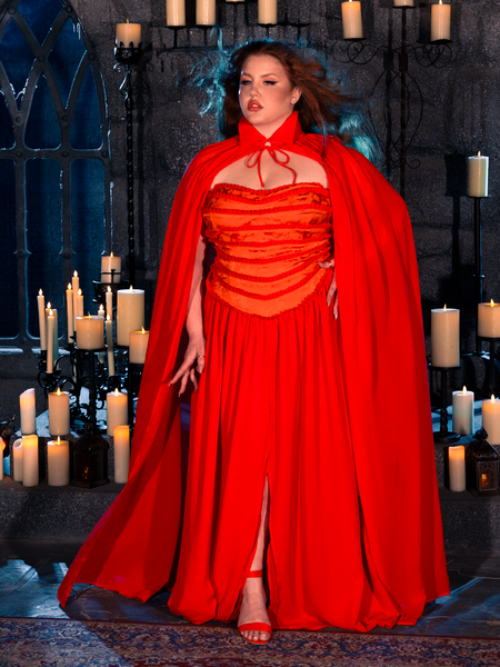 In a candlelit dungeon, a female model epitomizes gothic style, donning the BRAM STOKER'S DRACULA Lucy Bustier Gown and Matching Cape in Fire Orange, a remarkable creation from the gothic clothing collection of La Femme en Noir.