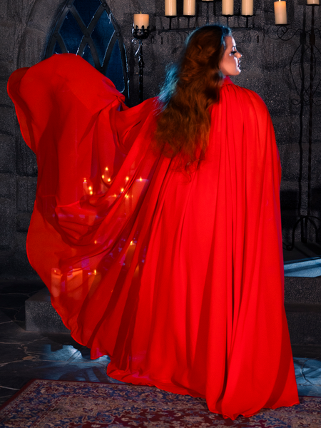 In a dimly lit dungeon, a female model showcases her elegant style with the BRAM STOKER'S DRACULA Lucy Bustier Gown and Matching Cape in Fire Orange, a captivating ensemble from the goth clothing brand La Femme en Noir.