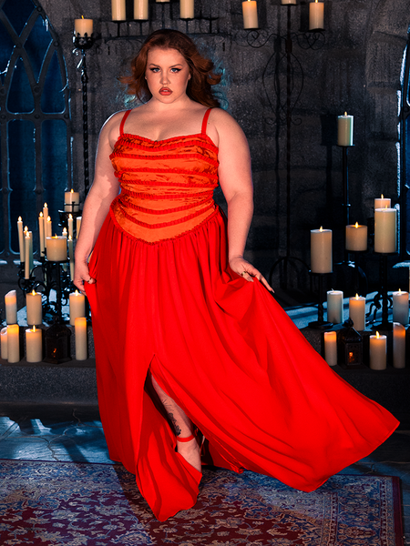 Dressed in the BRAM STOKER'S DRACULA Lucy Bustier Gown and Matching Cape in Fire Orange, a female model exudes the allure of gothic style within a candle-lit dungeon, thanks to the unique creations of La Femme en Noir, a prominent gothic clothing brand.