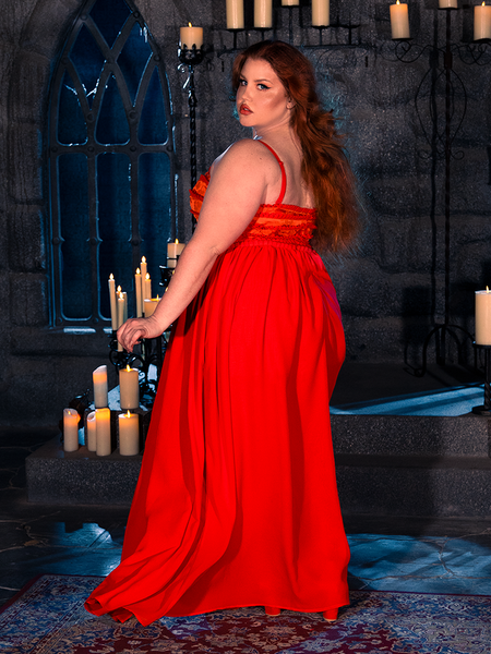 A female model captures the spirit of gothic clothing as she poses in a candle-lit dungeon, elegantly wearing the BRAM STOKER'S DRACULA Lucy Bustier Gown and Matching Cape in Fire Orange, a testament to La Femme en Noir's expertise in goth fashion.