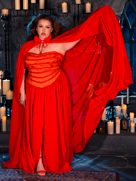 Wearing the BRAM STOKER'S DRACULA Lucy Bustier Gown and Matching Cape in Fire Orange, a female model embraces the ambiance of a candle-lit dungeon, showcasing the allure of gothic fashion from La Femme en Noir, the renowned gothic clothing label.
