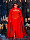 Dressed in the BRAM STOKER'S DRACULA Lucy Bustier Gown and Matching Cape in Fire Orange, a female model captures the essence of gothic clothing within the atmospheric setting of a candlelit dungeon, courtesy of La Femme en Noir's unique designs.
