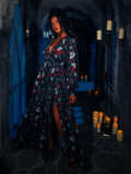 In a room illuminated solely by candles, the model confidently wears the BRAM STOKER'S DRACULA Belladonna Maxi Dress adorned with the Dracula Novelty Print.