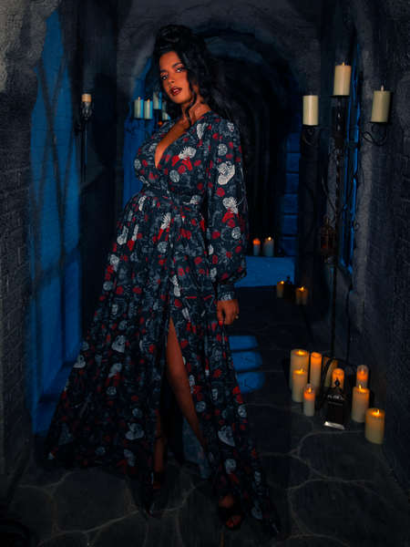 In a room illuminated solely by candles, the model confidently wears the BRAM STOKER'S DRACULA Belladonna Maxi Dress adorned with the Dracula Novelty Print.