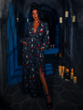 Amidst the haunting ambiance of a candlelit dungeon room, the model dons the BRAM STOKER'S DRACULA Belladonna Maxi Dress, showcasing its Dracula Novelty Print.