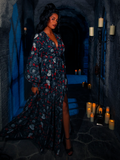 In a candle-lit dungeon room, the model elegantly showcases the BRAM STOKER'S DRACULA Belladonna Maxi Dress, adorned with Dracula Novelty Print.