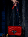 Embraced by the soft, eerie glow of candlelight, the BRAM STOKER'S DRACULA Gargoyle Sculpture Quilted Crossbody Bag in Blood Red is showcased, a masterpiece by the gothic artisans at La Femme en Noir.