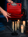 Amidst the flickering candlelight, the BRAM STOKER'S DRACULA Gargoyle Sculpture Quilted Crossbody Bag in Blood Red stands sentinel, a testament to the artistry of La Femme en Noir.