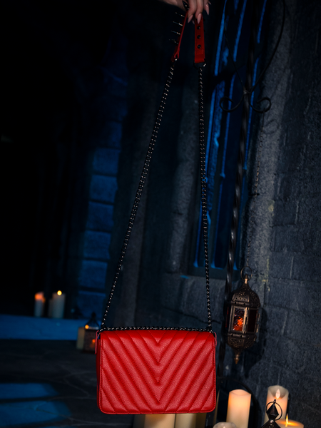 Bathed in the soft radiance of candle flames, the Gargoyle Sculpture Quilted Crossbody Bag in Blood Red, lovingly crafted by the gothic clothing brand La Femme en Noir, stands as a striking statement piece.